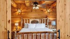 A wooden cabin bedroom with a bed, a ceiling fan, and wall-mounted lights. - Buffalo Lodge – Stay for 6 (Branson)