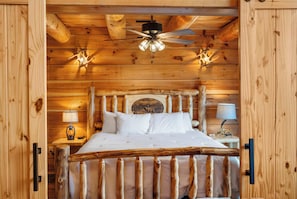 A wooden cabin bedroom with a bed, a ceiling fan, and wall-mounted lights.