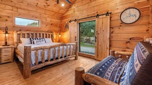 A wooden cabin bedroom with a bed, a bench, a wall clock, and a window.