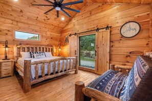 A wooden cabin bedroom with a bed, a bench, a wall clock, and a window.