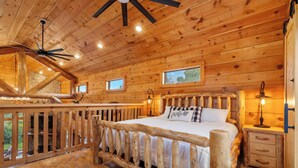 A wooden cabin bedroom with a bed, a nightstand, a lamp, and a ceiling fan. - Antler Summit Trio – For 14 (Branson)