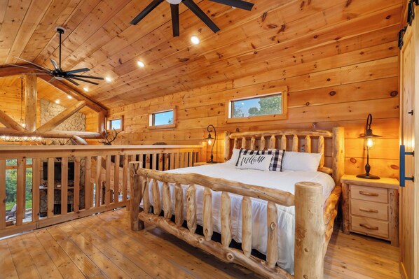 A wooden cabin bedroom with a bed, a nightstand, a lamp, and a ceiling fan. - Antler Summit Trio – For 14 (Branson)