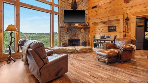 A log cabin interior with a stone fireplace, leather furniture, and a television mounted on the wall. - Antler Summit Trio – For 14 (Branson)
