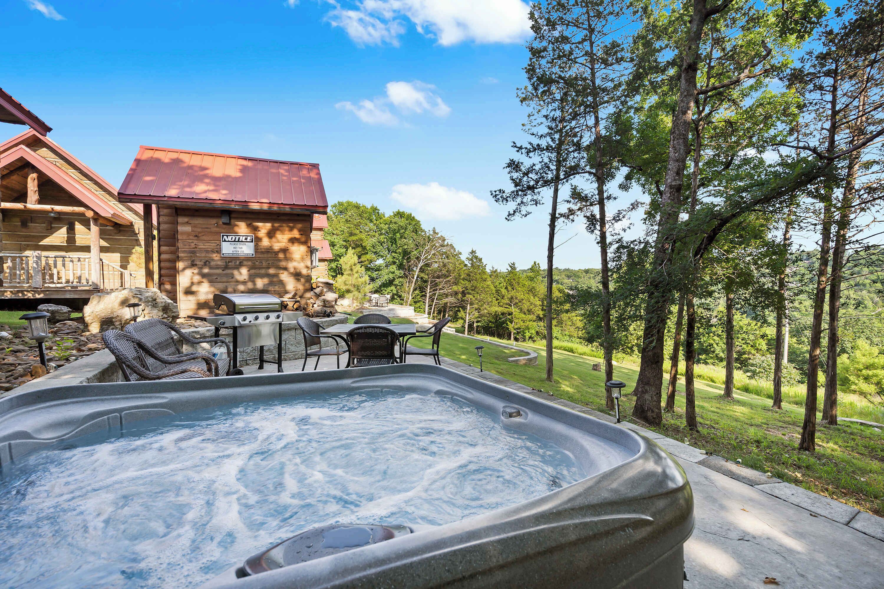 A hot tub with outdoor furniture, a wooden cabin, and a forested area.
