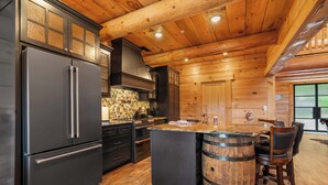 A modern kitchen with a large refrigerator, wooden cabinets, and a bar area with stools. - Antler Summit Trio – For 14 (Branson)