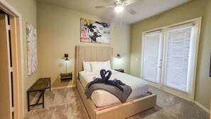 Una camera da letto con un letto, lampade sui comodini, una ventola a soffitto, una panca e una porta.