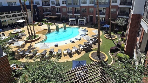 A rooftop pool with sun loungers and palm trees, surrounded by a modern building with balconies.
