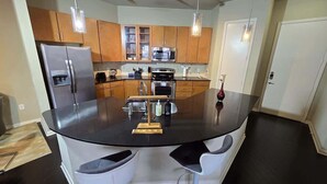 A modern kitchen with a central island, stainless steel appliances, wooden cabinets, and pendant lighting.