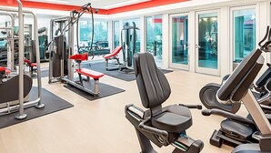 Ein modernes Fitnessstudio mit unterschiedlichen Trainingsgeräten, großen Fenstern und Deckenventilatoren.
