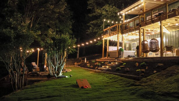 Una casa de dos pisos con un balcón, mobiliario exterior e iluminación colgante.