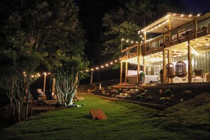 Een twee verdiepingen tellend huis met een terras, zitplaatsen buiten en lichtjes.