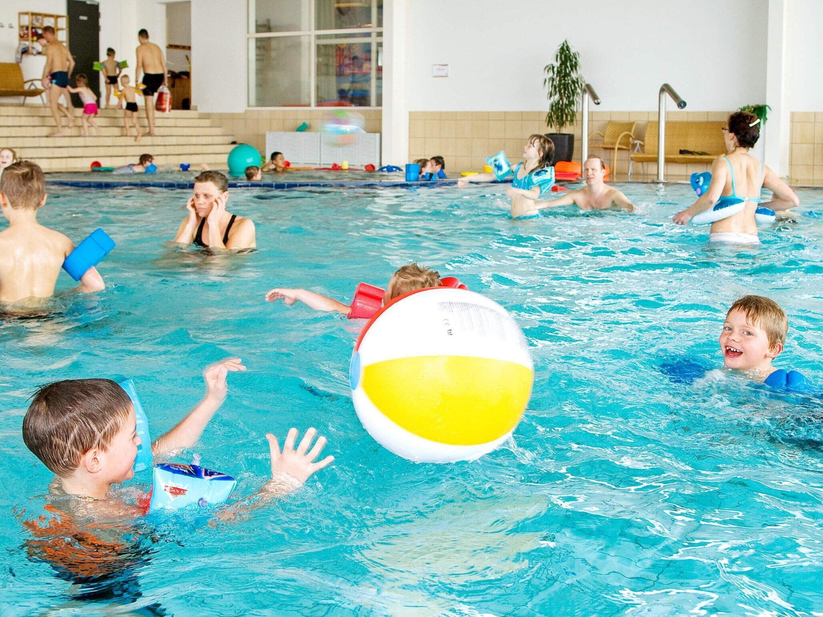 An indoor swimming pool with multiple people swimming and playing.