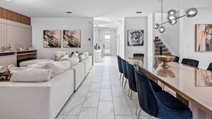 A modern kitchen with white cabinetry, a central island, and a dining area with a long table and blue chairs.