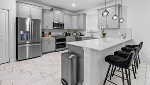 A modern kitchen with stainless steel appliances, white cabinetry, and a bar area with black stools.