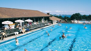 Une piscine avec plusieurs couloirs de nage, des spectateurs et des parasols.