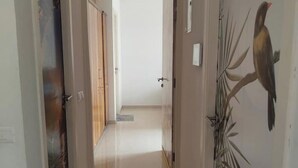A hallway with a wooden door on the left, a white door in the center, and a wall with a bird mural on the right. - Spacious 1BHK Hiranandani Estate (Thane)