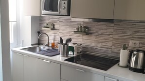 A modern kitchen with white cabinets, a stainless steel sink, a microwave, and a kettle.