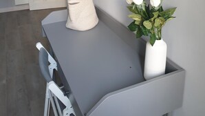 A modern room with a grey desk, a white vase with flowers, a white towel, and a door in the background.