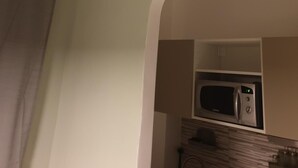 A kitchen with a white air conditioner mounted on the wall, a microwave, and a wooden cabinet below.