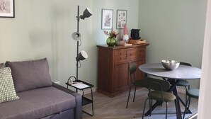 A living room with a sofa, a dining table with chairs, a cabinet, and a pendant light.