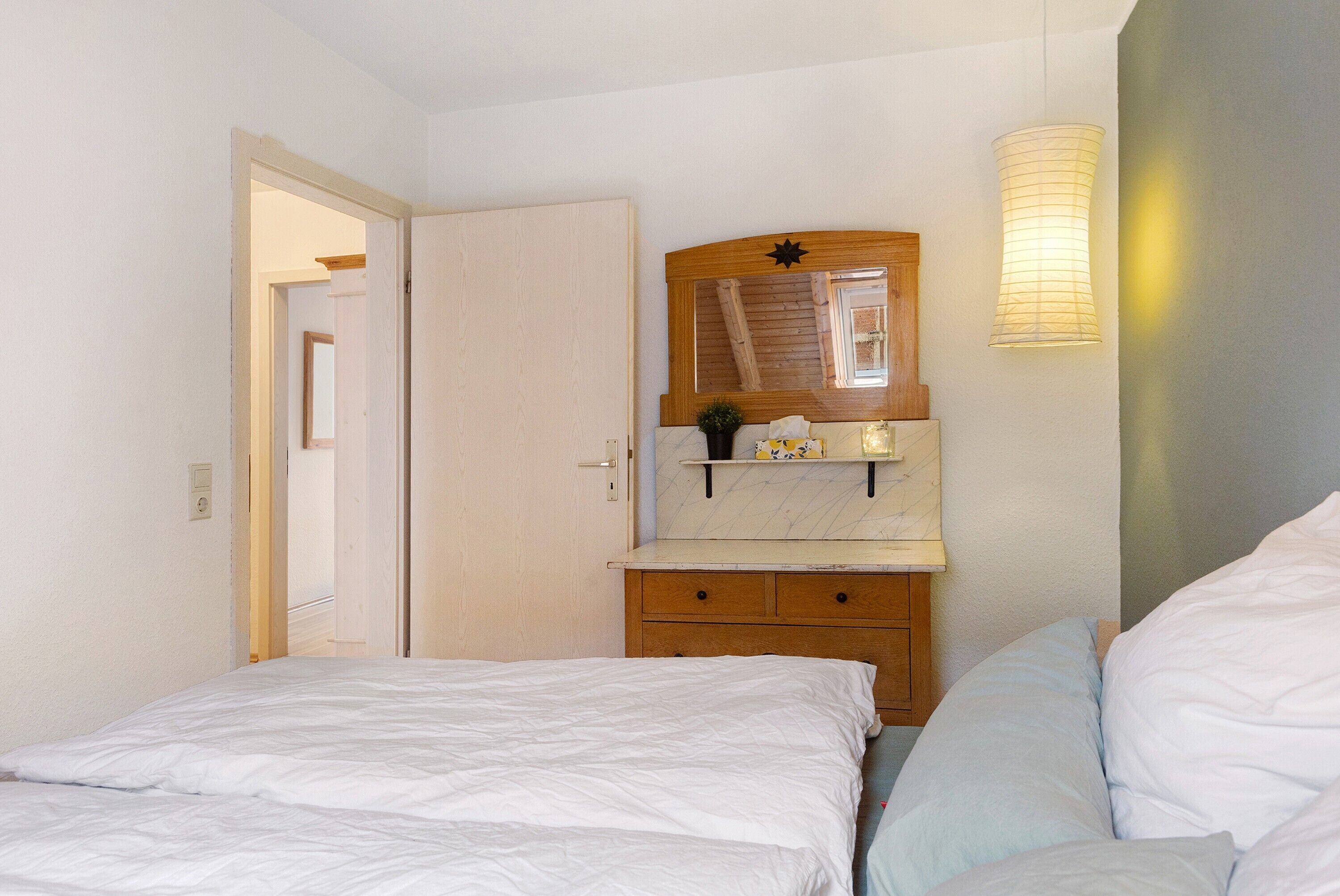 A bedroom with a bed, a nightstand, a dresser, a mirror, and a wall-mounted light fixture.