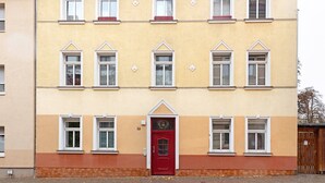 A multi-story building with a red door, multiple windows, and a brick-paved ground.