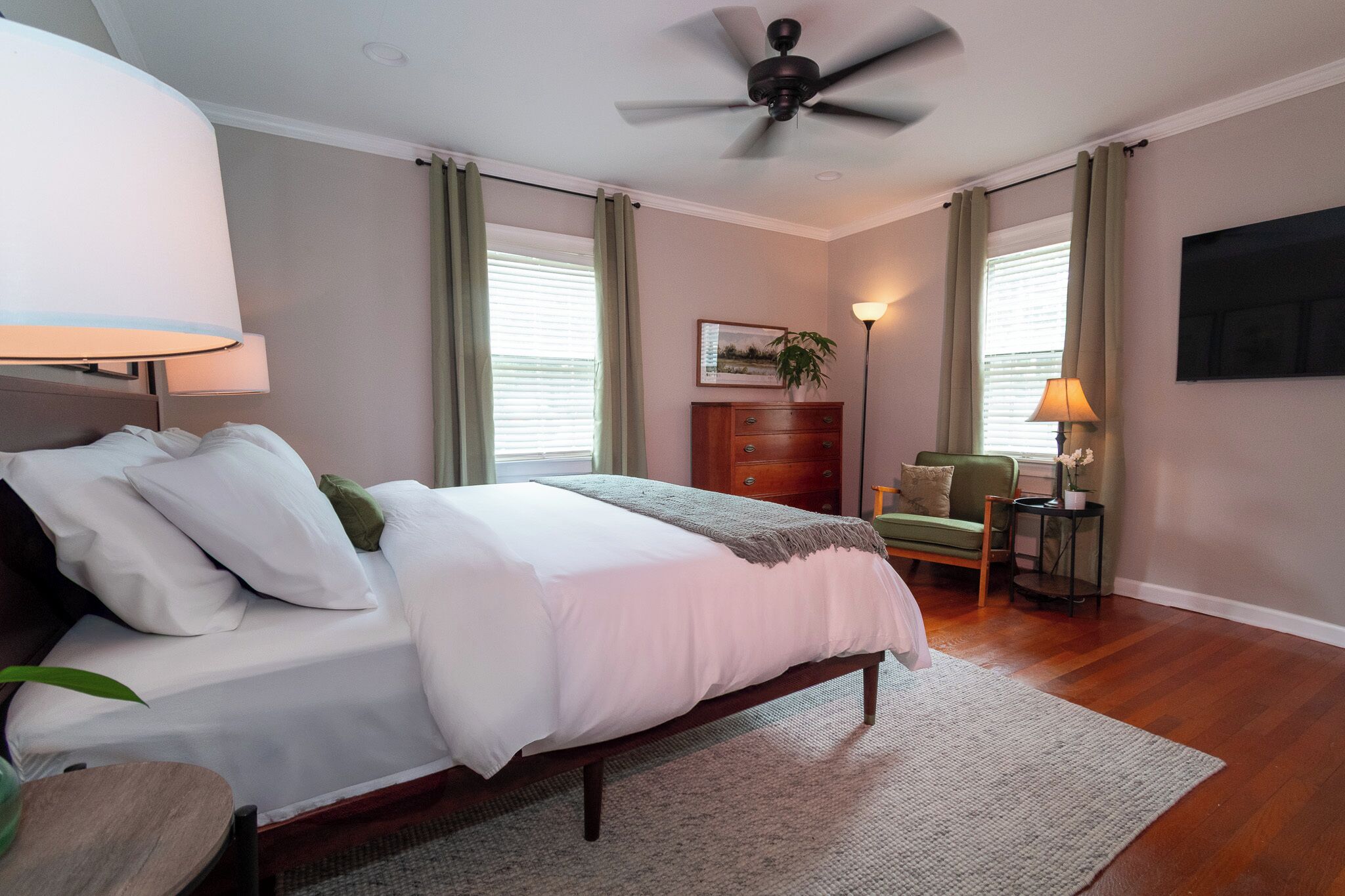 Een slaapkamer met een bed, een plafondventilator, een bureau, een stoel, een lamp en een plant.