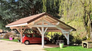 Un espace de stationnement couvert où une voiture rouge est garée sous une structure en bois.