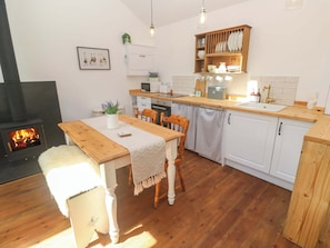 A cozy kitchen with wooden cabinets, a dining table with chairs, a fireplace, and a hanging light fixture.