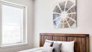 A bedroom with a bed, a window with blinds, and a wall-mounted artwork.