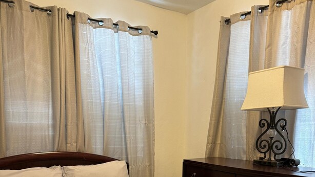A neatly made bed with a green quilt, a white pillow, and a folded white towel on the bed. There is a dark wooden dresser with a lamp on top to the right. - 30 Day Minimum-3BR in Santurce-Near Beach UNIT 1 (San Juan)