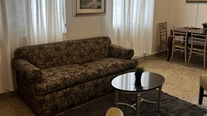 A living room with a patterned sofa, a round coffee table, a yellow armchair, a dining table with chairs, and two framed pictures on the walls. - 30 Day Minimum-3BR in Santurce-Near Beach UNIT 1 (San Juan)