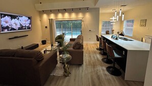 Un salon moderne avec un canapé, une table basse et un téléviseur. Il y a également un coin cuisine équipé d’un bar et d’un évier.