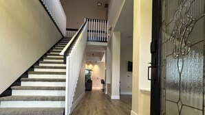 Un couloir au plancher de bois, avec un escalier sur la gauche et une porte à cadre noir sur la droite.