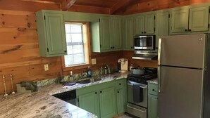 Una cocina con gabinetes verdes, un refrigerador de acero inoxidable, un microondas, una estufa y un lavamanos.