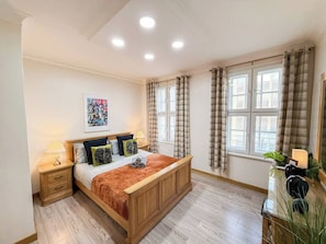 Een slaapkamer met een houten bed, nachtkastjes, een bureau en een raam met gordijnen.