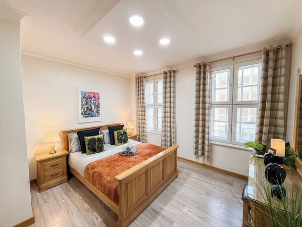 Une chambre à coucher avec un lit en bois, des tables de chevet, un bureau et une fenêtre avec des rideaux.