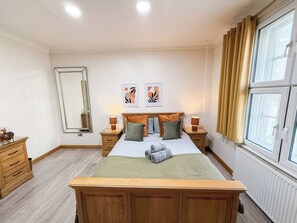 Een slaapkamer met een houten bed, twee nachtkastjes, een spiegel en een raam met gordijnen.