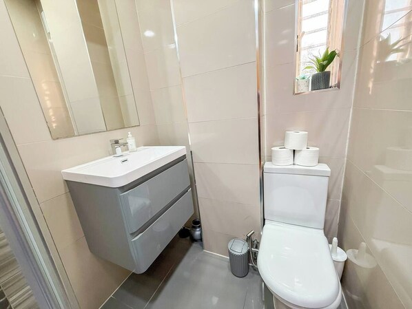 Une salle de bain avec un lavabo blanc, des toilettes et une petite fenêtre agrémentée d’une plante.