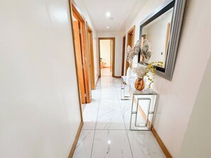 Un couloir avec des portes en bois, un sol en marbre et un miroir au mur.