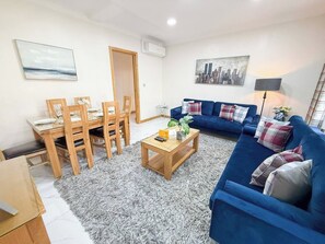 Un salon avec un canapé bleu, une table à manger en bois et des chaises.