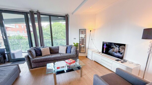 Una sala de estar moderna con un sofá, una mesa de centro, un televisor y un balcón con ventanas amplias.
