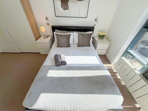 Habitación de hotel con cama, mesita de noche, lámpara y ventana con vistas.