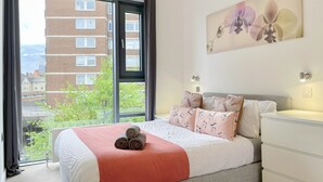 Un dormitorio con un ventanal grande, una cama con una colcha rosa y una obra de arte colgada en la pared.