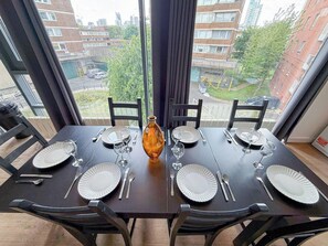 Mesa de comedor lista para cuatro personas, con platos, cubiertos y un florero.