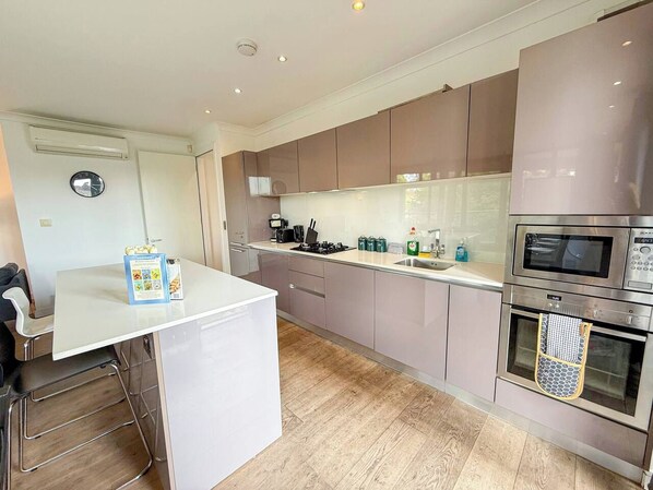 A modern kitchen with stainless steel appliances, a white countertop, and wooden flooring.