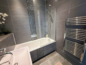 A modern bathroom with a bathtub, a glass shower enclosure, and a towel rack.