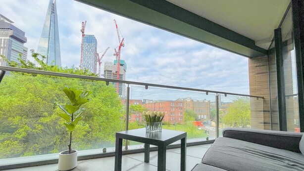 Un balcón con vista a un paisaje urbano, que incluye edificios modernos y grúas de construcción.