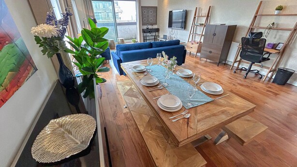 A dining area with a wooden table set for four, a blue sofa, and a large plant.