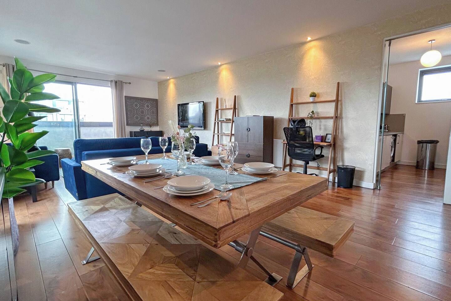 A dining area with a wooden table set for four, a blue sofa, and a TV mounted on the wall.
